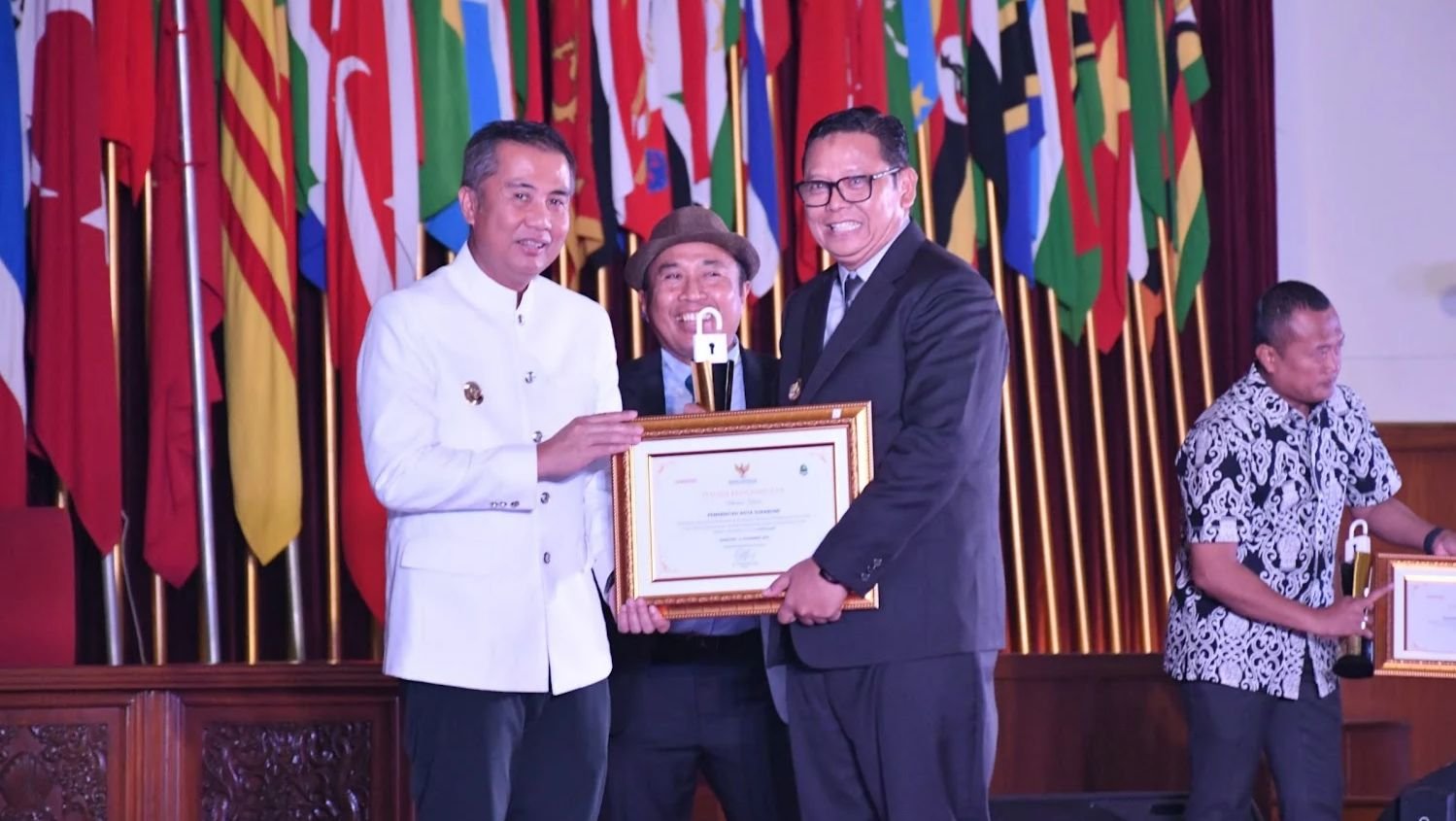 Pj Gubernur Jawa Barat, Bey Triadi Machmudin, menyerahkan penghargaan badan publik informatif kepada Pj Wali Kota Sukabumi, Kusmana Hartadji, dalam acara anugerah keterbukaan informasi publik. Foto: Dokpim Kota Sukabumi.